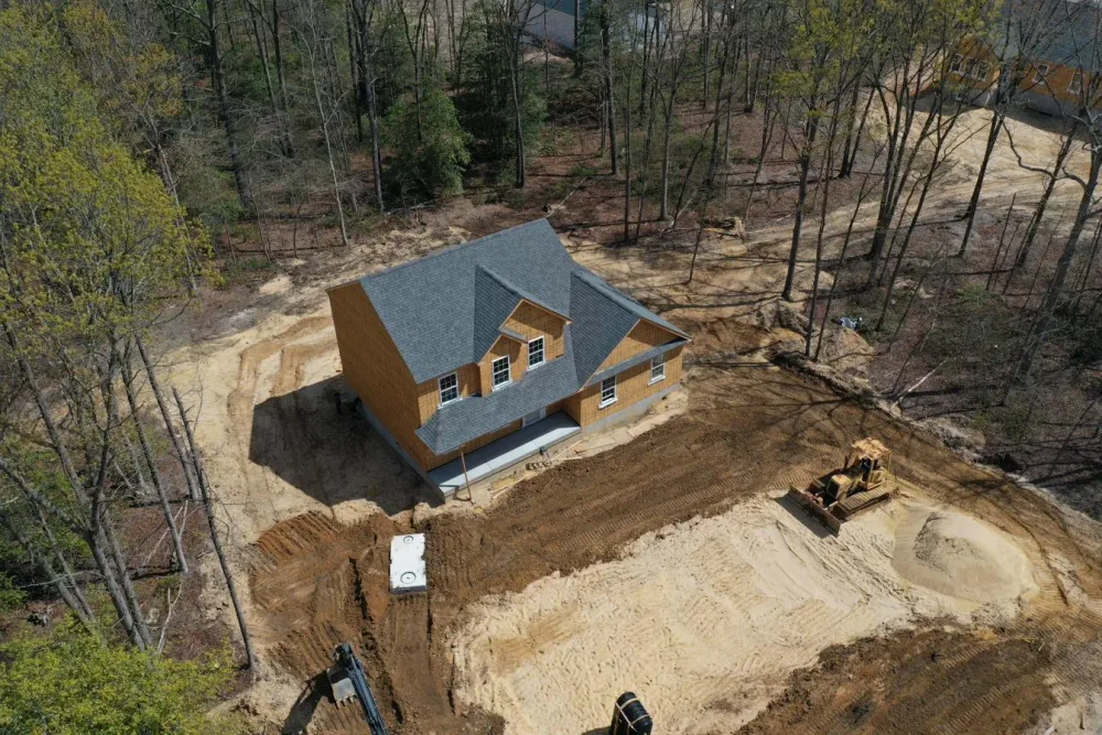New construction colonial under roof framing at a South Jersey homesite — drone view showing graded lot, septic install, and site work in progress